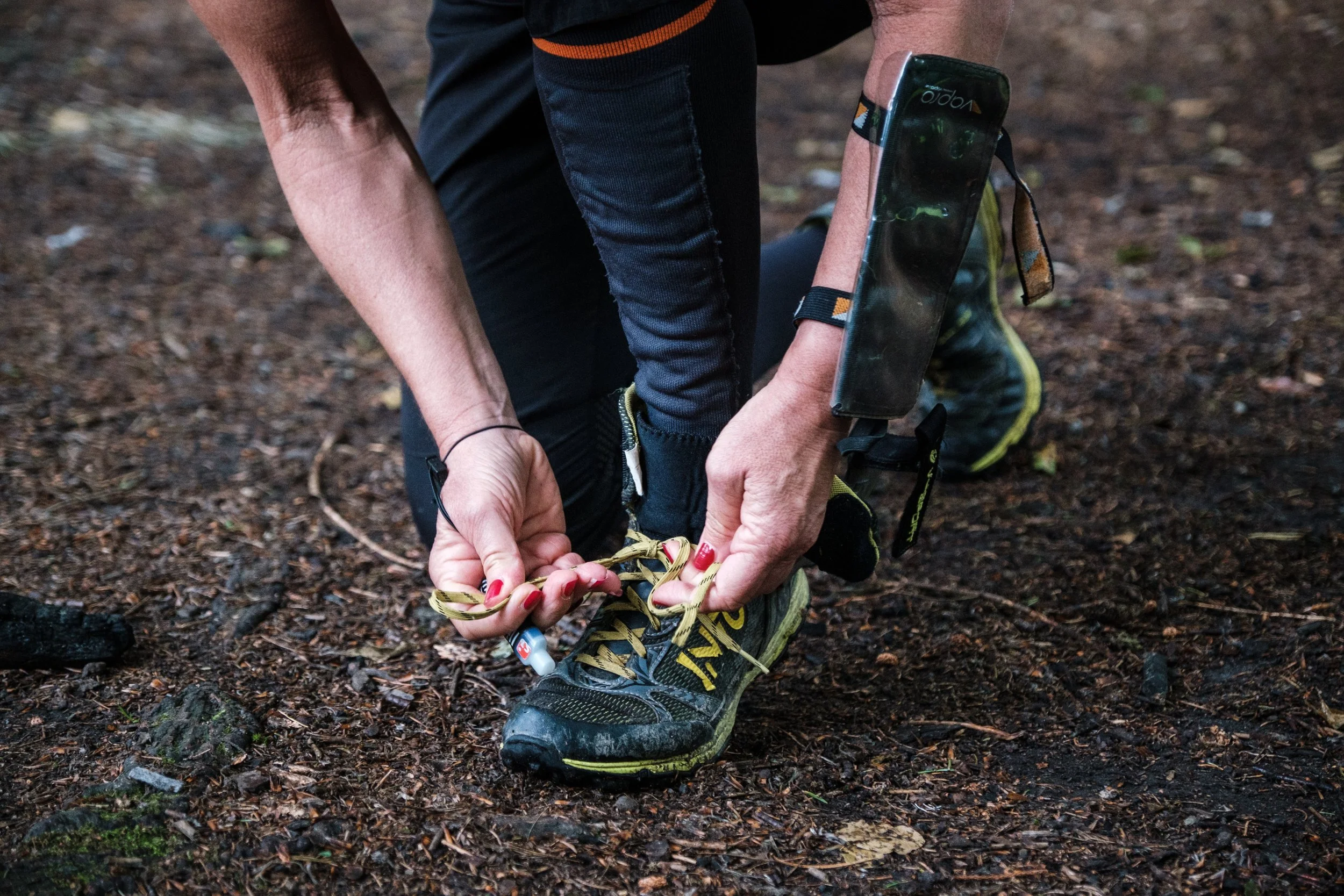 Eine Person bindet die Schnürsenkel ihrer Wanderschuhe auf einem Waldboden.