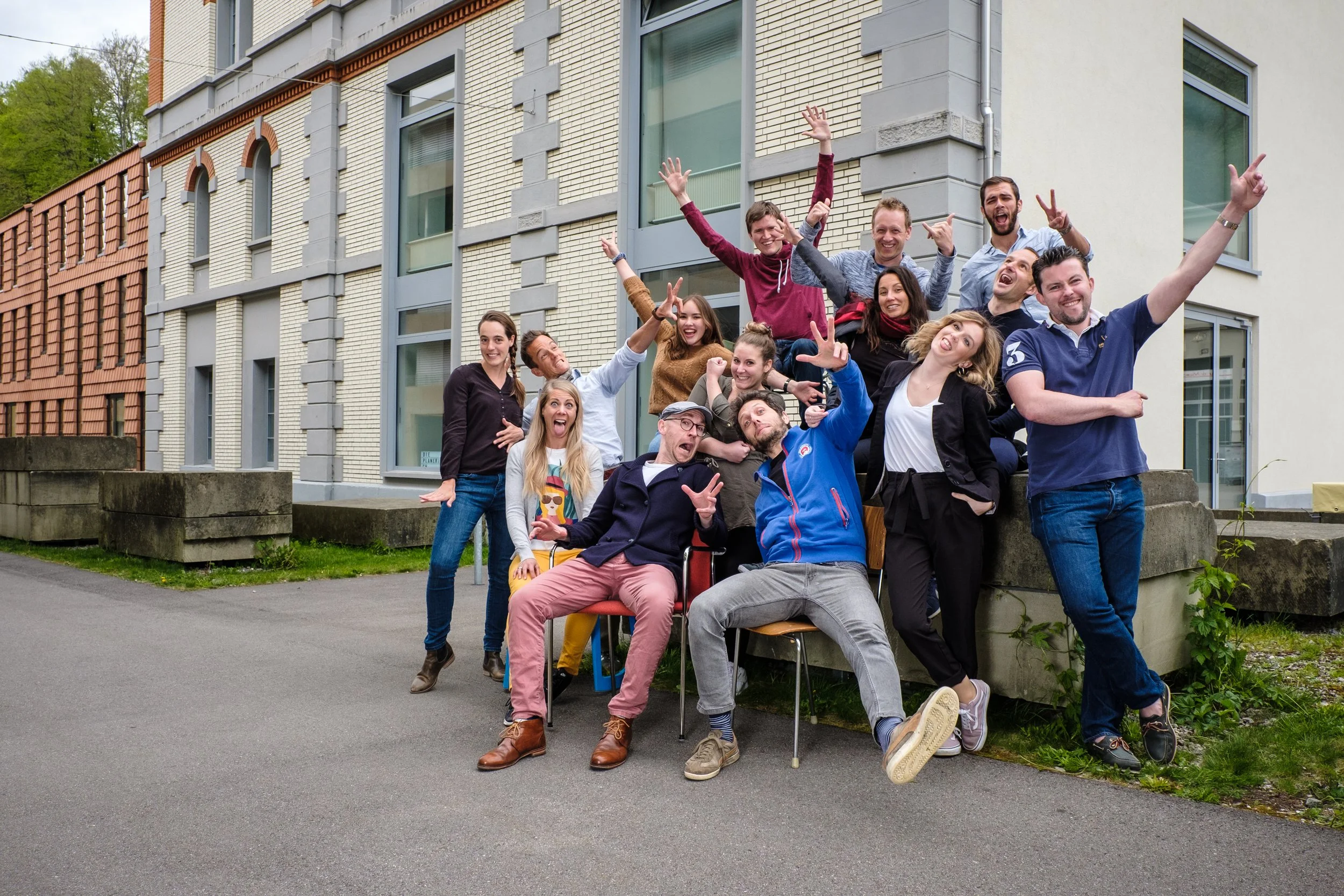 Gruppe von jungen Menschen, die vor einem modernen Gebäude draußen zusammen lachen und posieren für ein Foto.