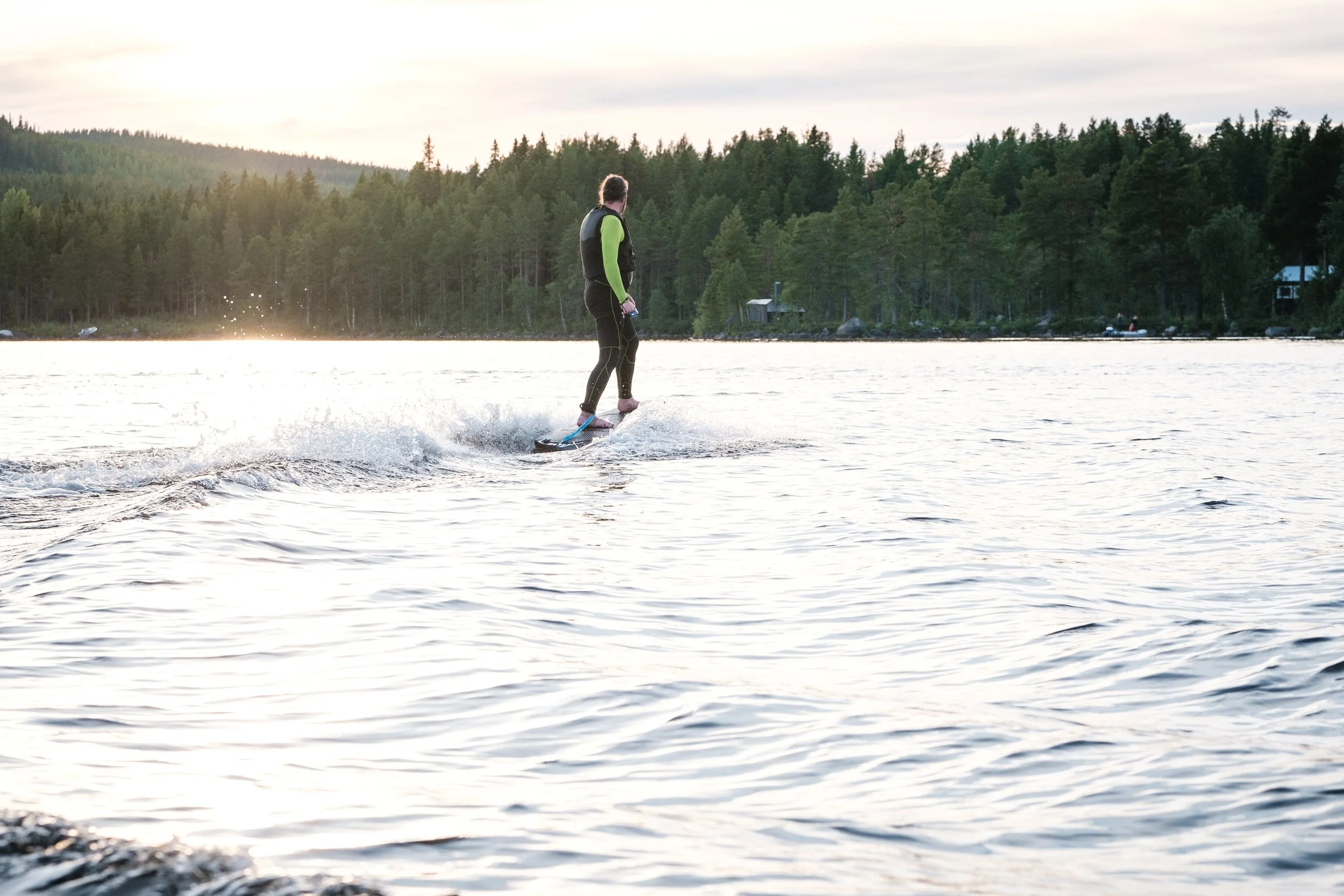 Person beim Wasserskifahren auf einem See bei Sonnenuntergang, umgeben von Wald.