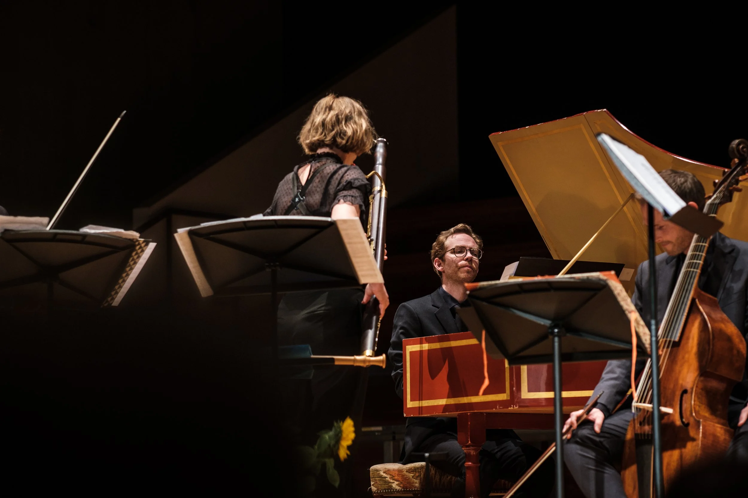 Musiker bei einem klassischen Konzert spielen auf einer Bühne, mit Flöte, Klavier, Cello und Notenständern.
