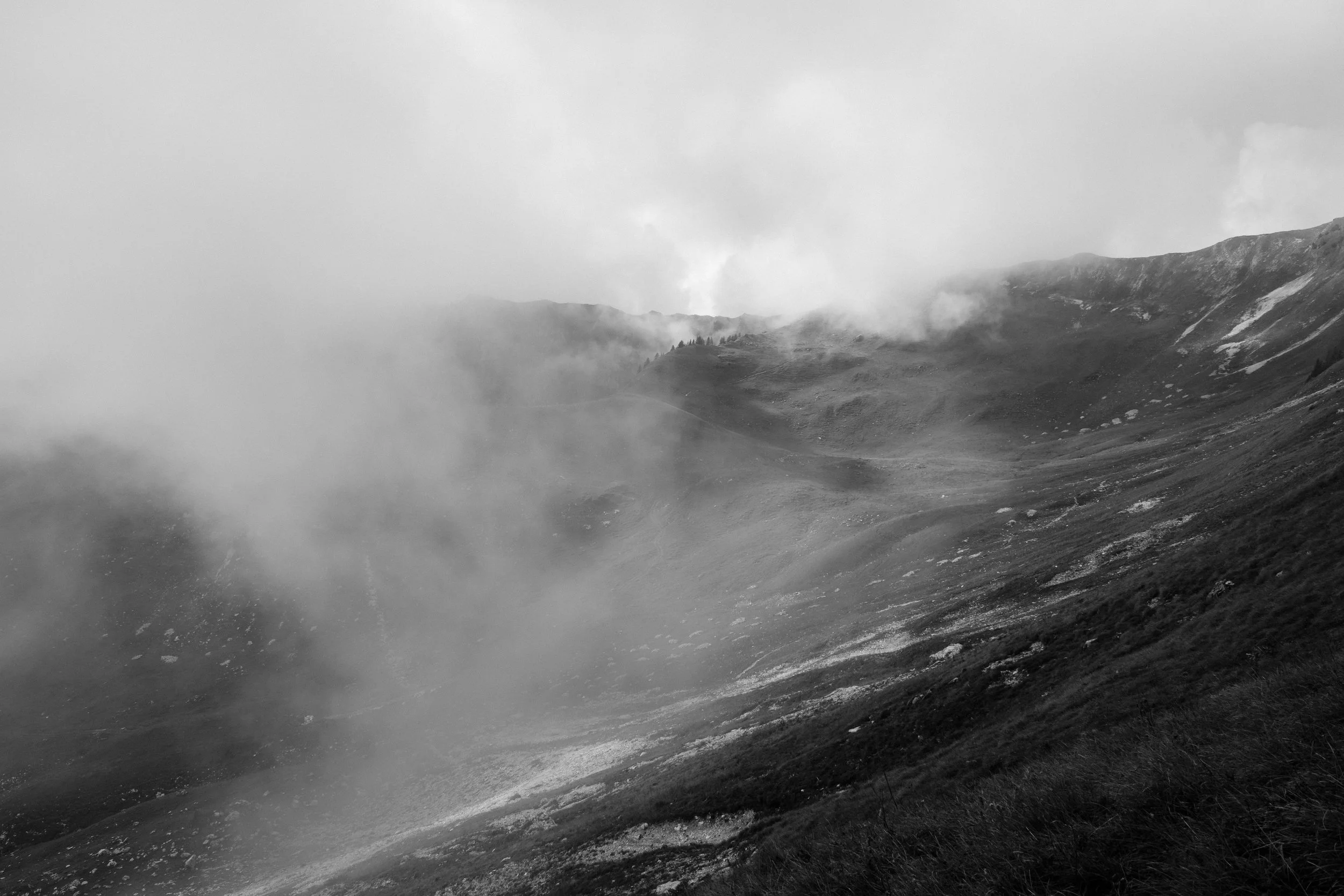 Berglandschaft im Nebel mit Steigungen und Wolken über den Gipfeln, schwarz-weißes Foto