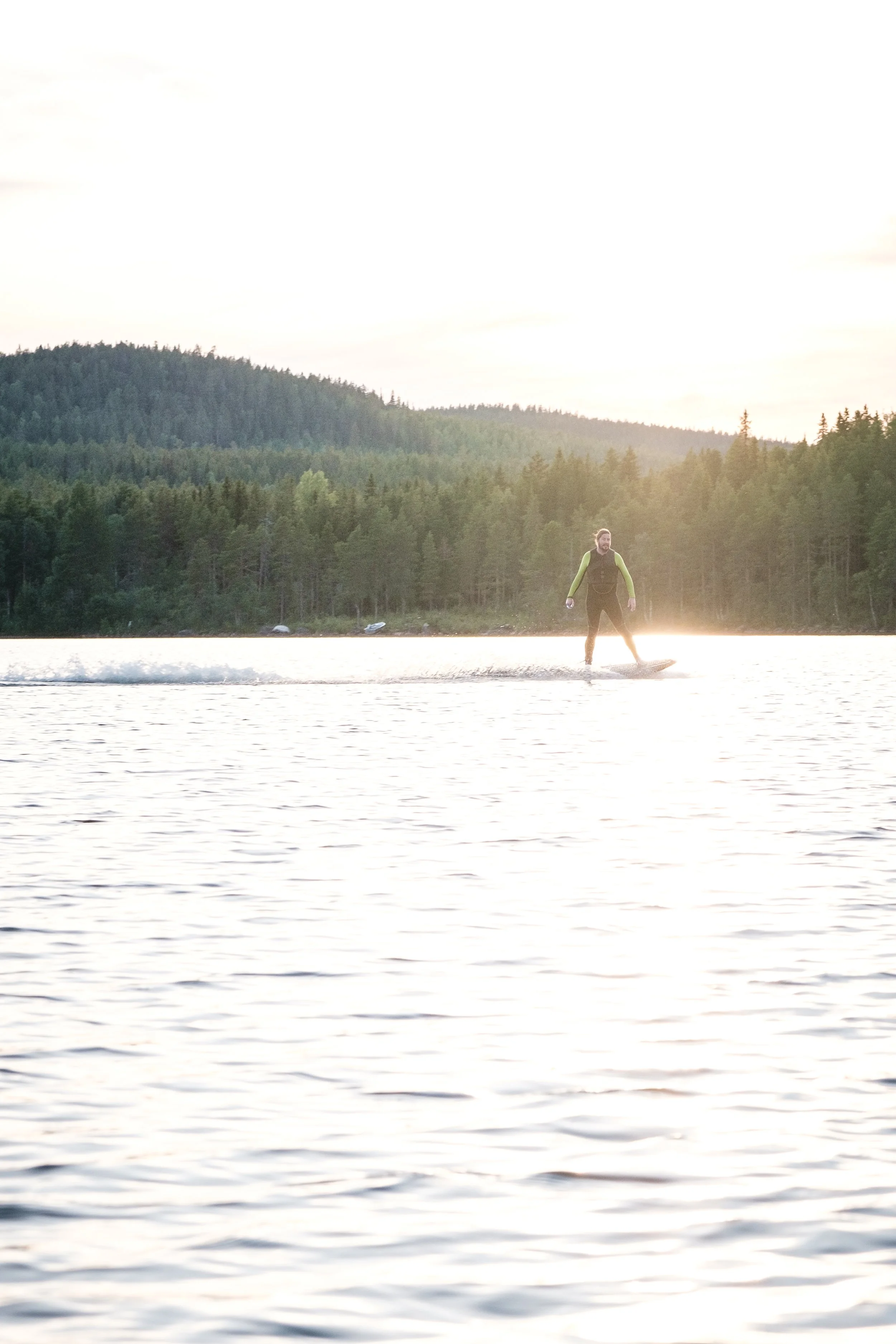 Person beim Wasserski auf einem See mit Wald im Hintergrund bei Sonnenuntergang.
